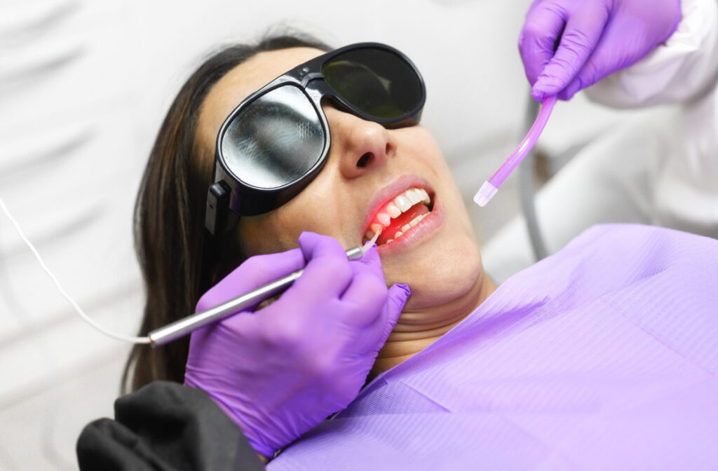 A dentist with a violet coloured latex glove using a dental laser on her patient's teeth.
