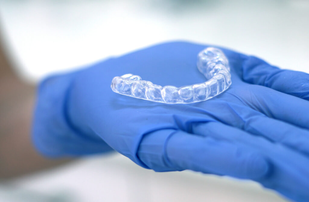 A clear aligner sitting on a blue-gloved hand.