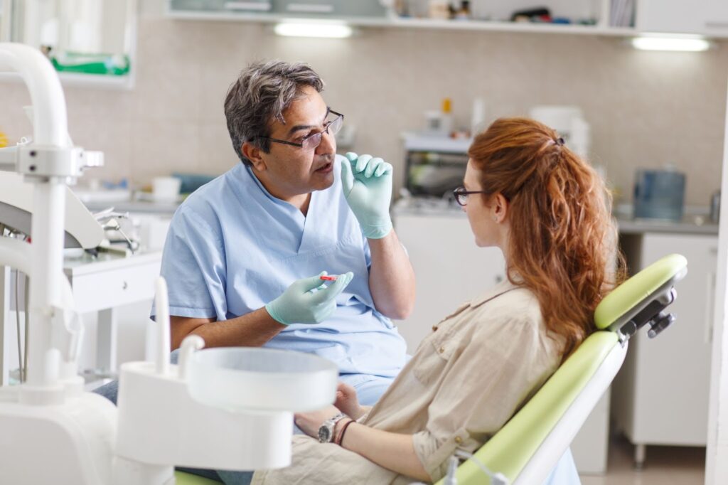 A dentist explains a procedure to a female patient in the dentist's chair.
