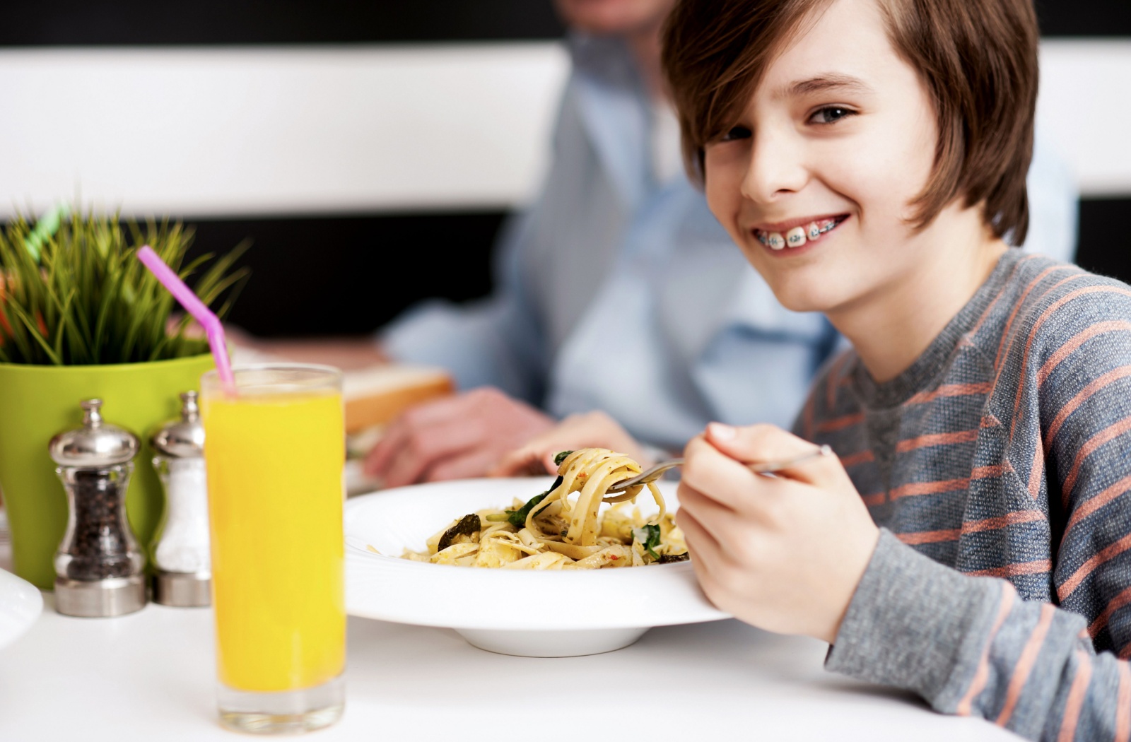 A smiling boy with braces enjoys a plate of soft pasta.