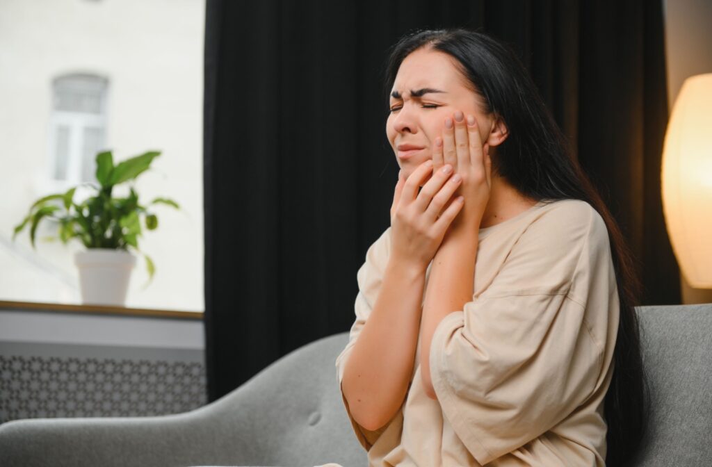 A young adult holding the side of their face winces in pain, suspecting they may have an abscessed tooth.