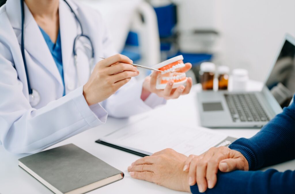 A dentist using a model of the human mouth to describe to a patient what to expect from their procedure after dental freezing.