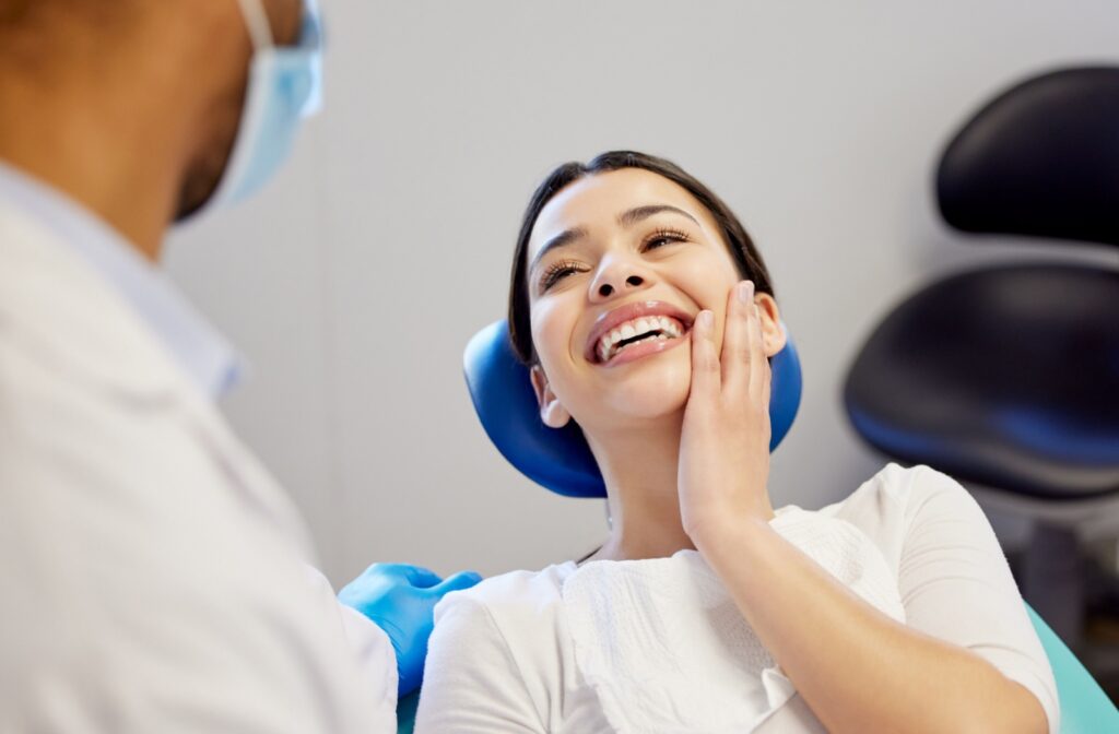 A patient rubbing their jaw after laser dentistry and smiling at their dentist.