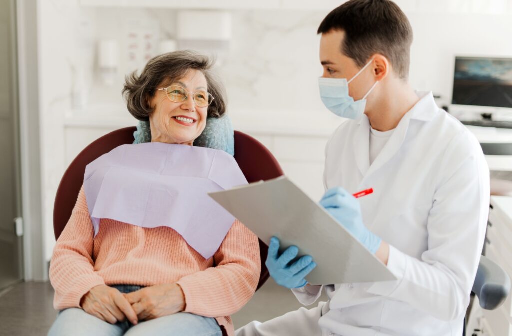 A dentist writes notes on a clipboard while talking to a dental patient during an examination.