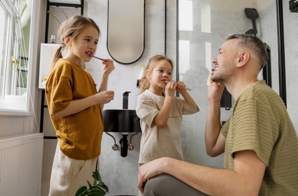 A parent and their two children brush their teeth together, practicing proper brushing technique.