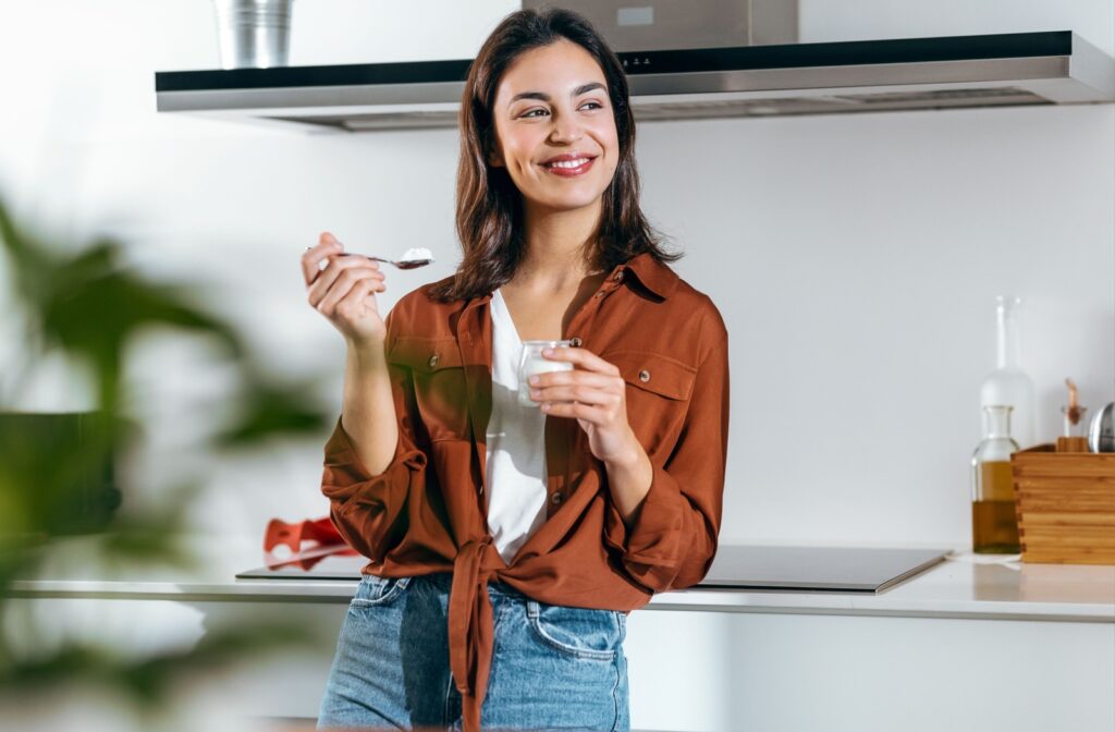 A person smiles as they eat yogurt in a bright kitchen after a dental cleaning.