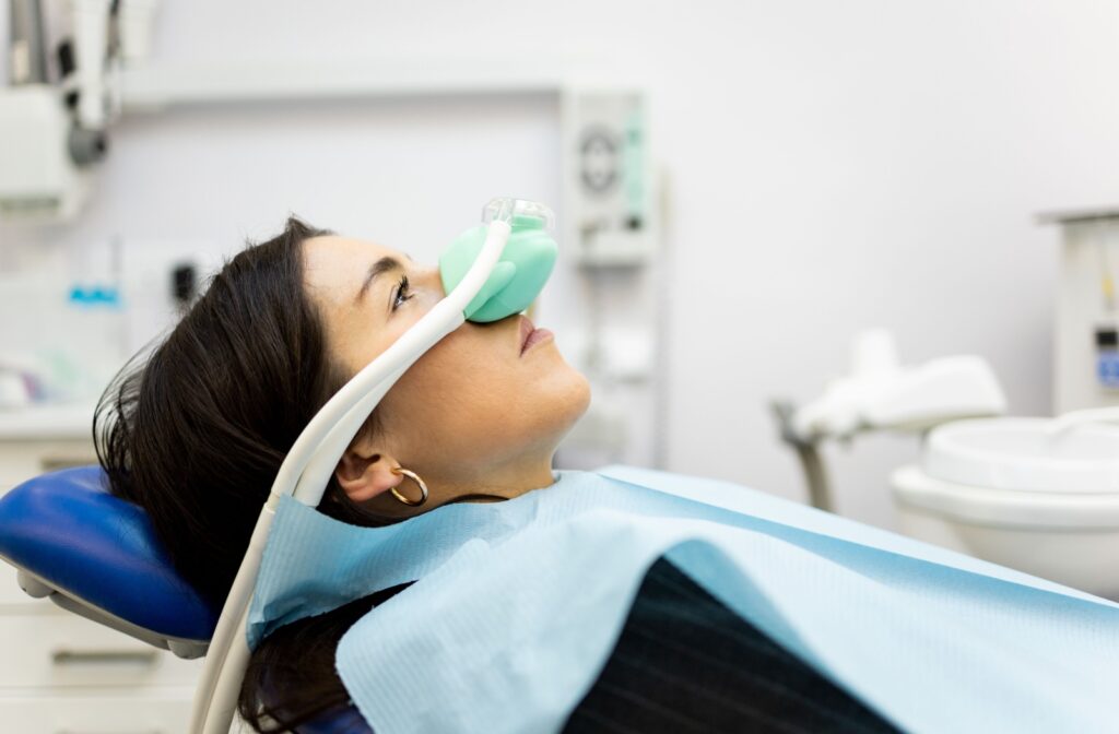 A person lying back in a dental chair wearing a green nosepiece for nitrous oxide sedation.