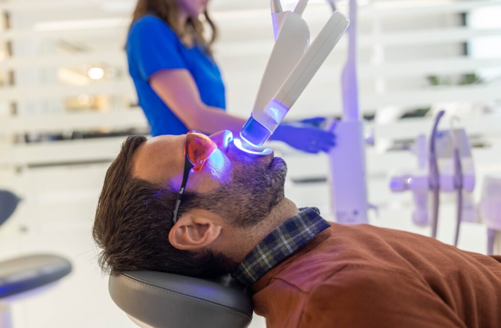 An adult lies back in their dentist's chair as they undergo an in-office teeth whitening treatment.