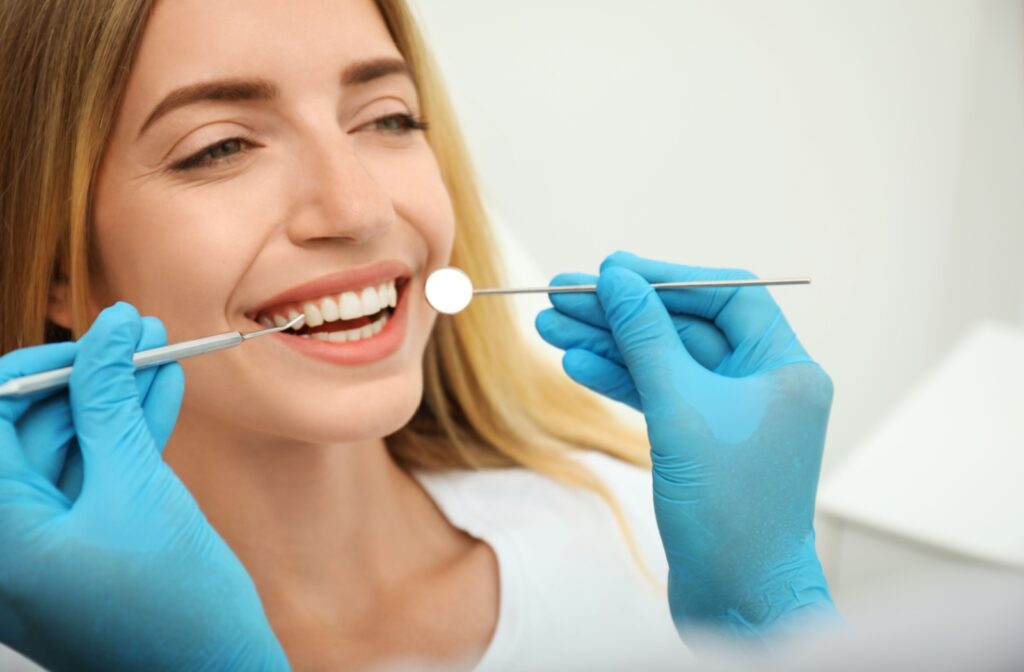 2 hands in blue gloves holding dental instruments to a smiling person's teeth.