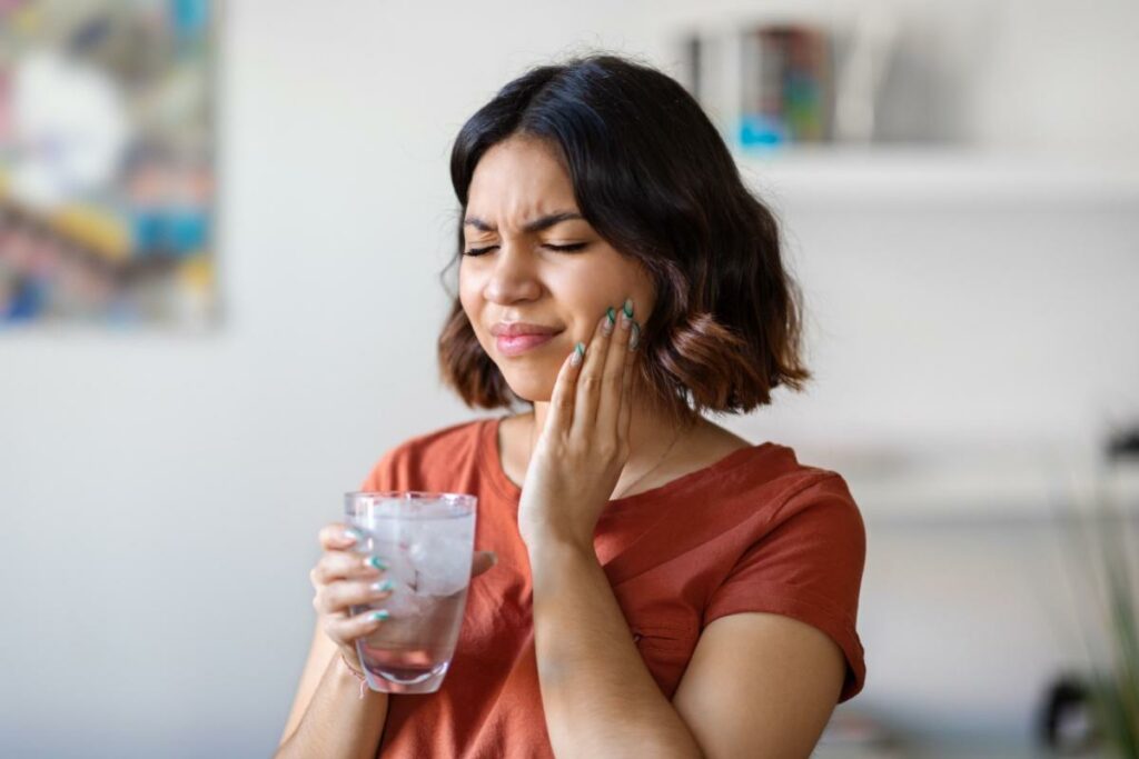 Woman holding a glass of water and her right jaw in pain.